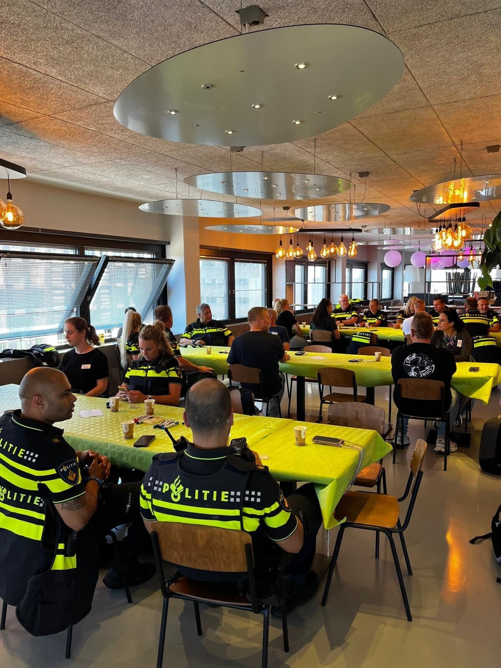 Groep mensen, waaronder politieagenten, aan tafel in een groot, gezellig ingerichte ruimte.