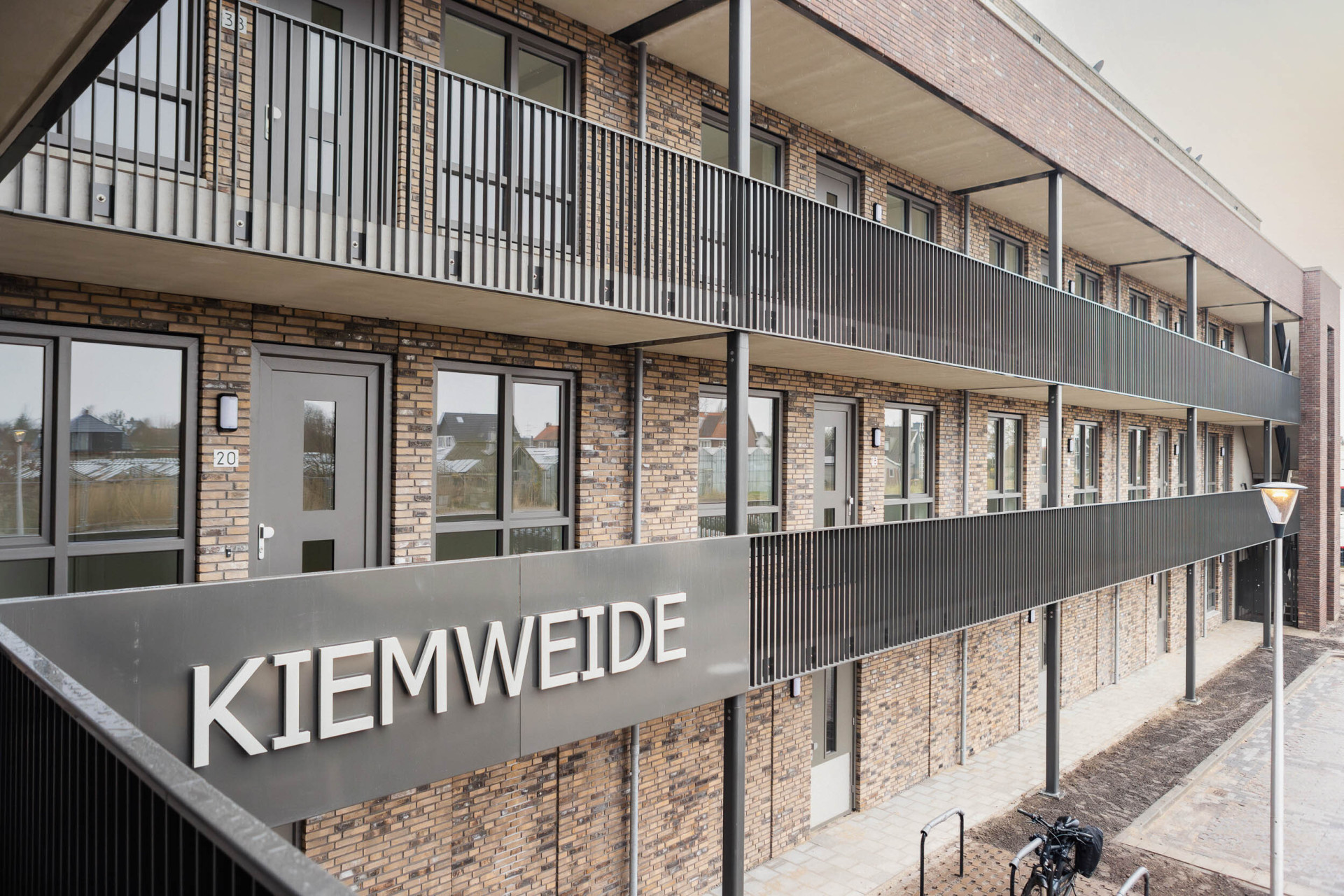 Appartementencomplex genaamd "Kiemweide" met bakstenen gevel en metalen balkons.