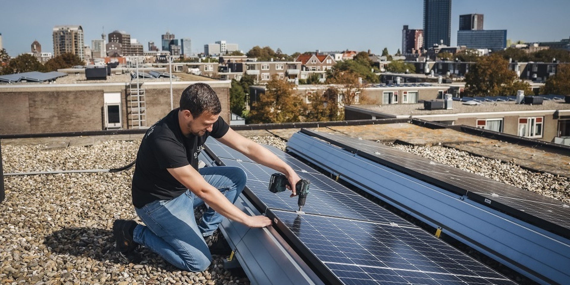 Man installeert zonnepanelen op een dak in een stedelijke omgeving.