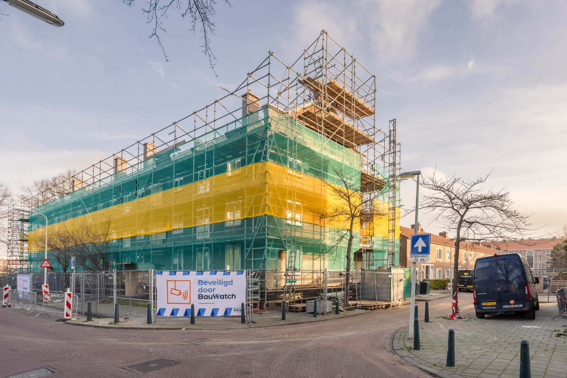Bouwplaats van een gebouw met steigers en kleurrijke netten.