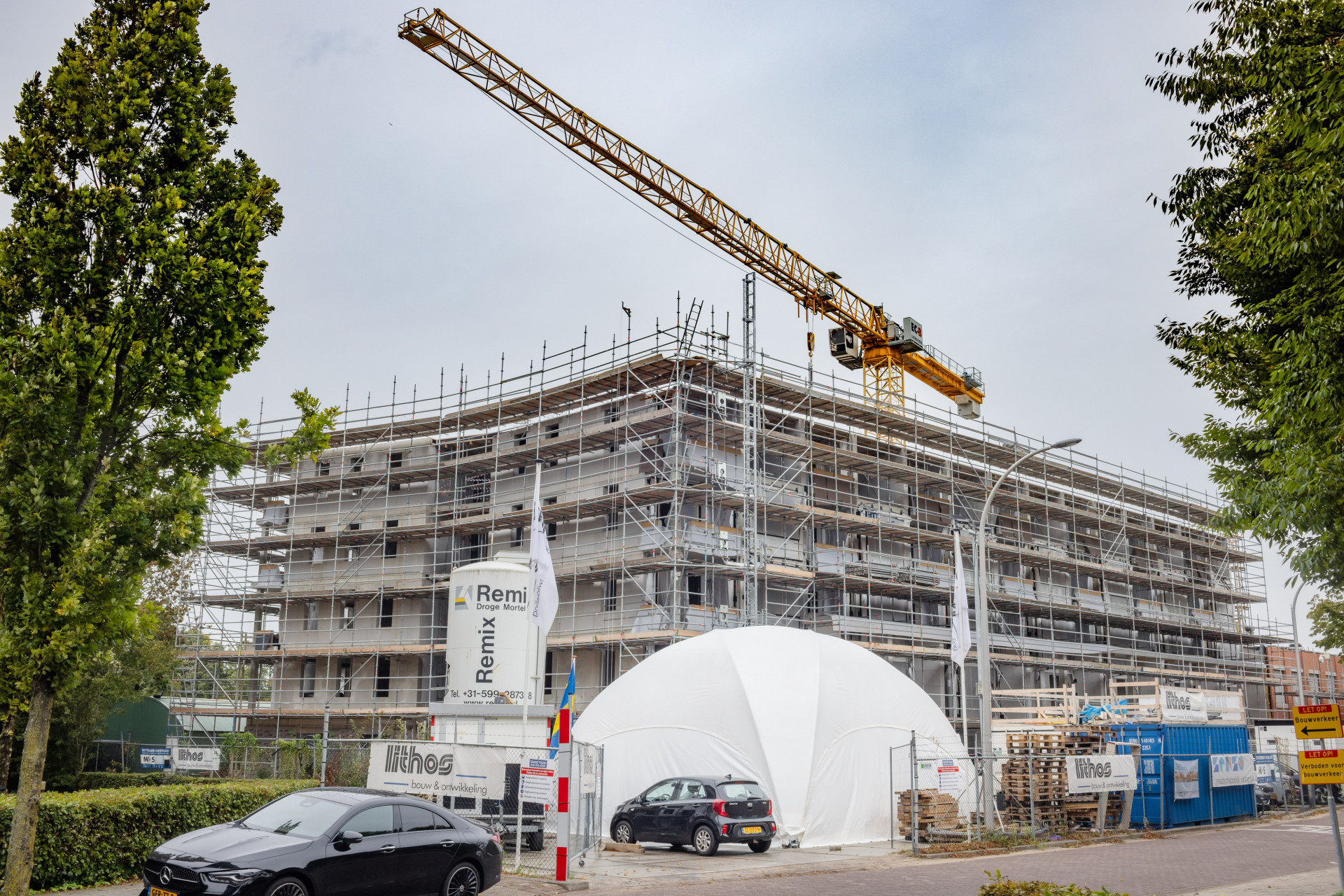 Nieuwbouwplaats met hijskraan en steigers.