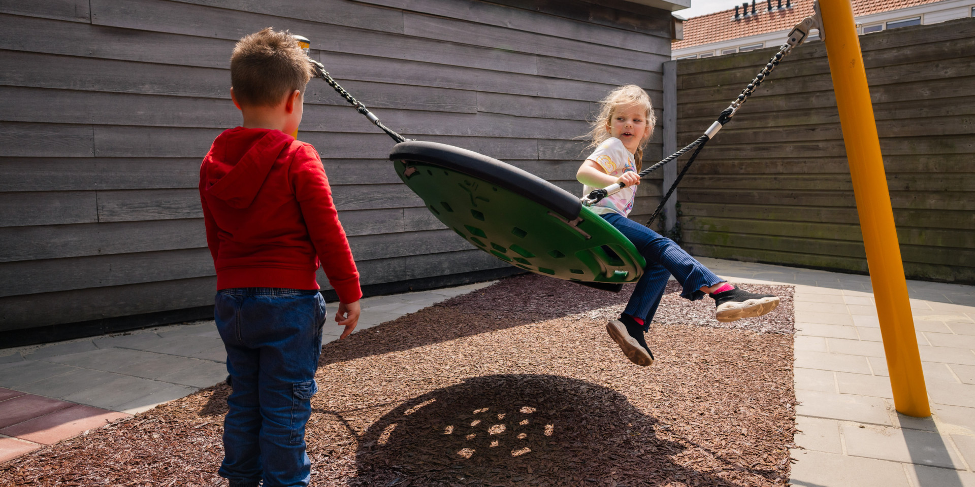 Twee kinderen spelen op een schommel in de zon.