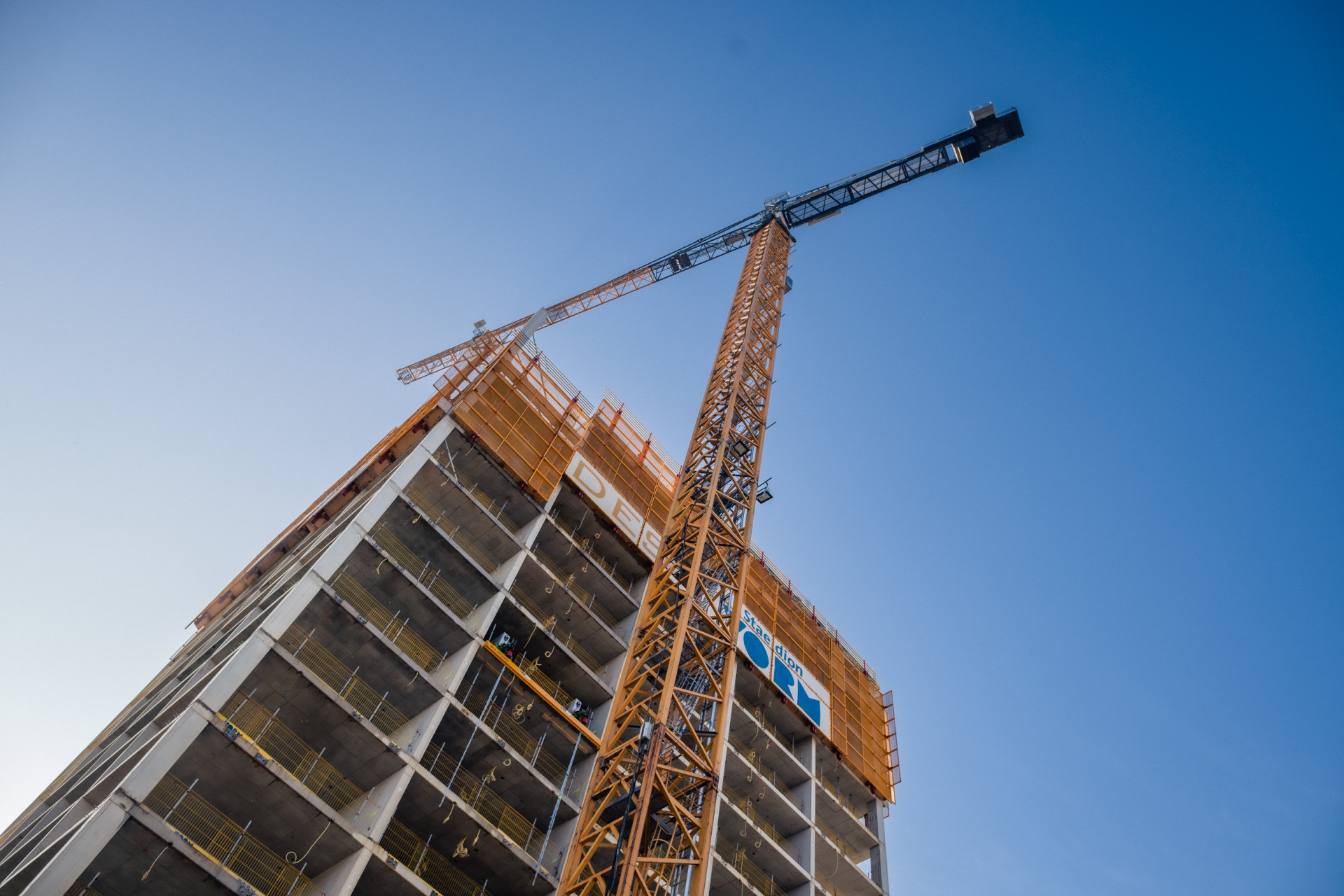 Bouw van een hoog gebouw met hijskraan tegen een blauwe lucht.