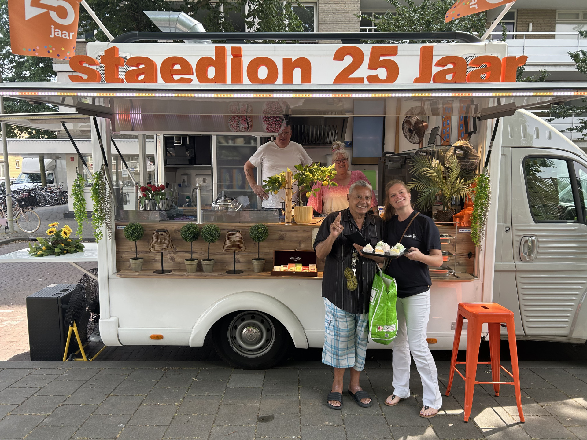 Mensen poseren voor een foodtruck met het opschrift "Staedion 25 jaar".
